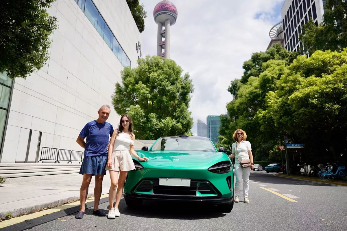 Three people beside a green electric car near the Oriental Pearl Tower in Shanghai